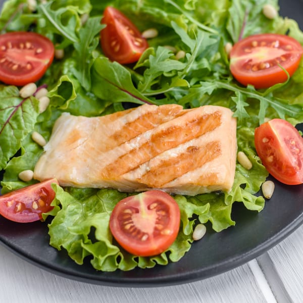 Grilled salmon fillet on a bed of fresh green lettuce and arugula with cherry tomatoes and pine nuts.