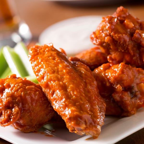 Close-up of Twin Acres-19th Hole's buffalo wings coated in sauce, with celery and dip.