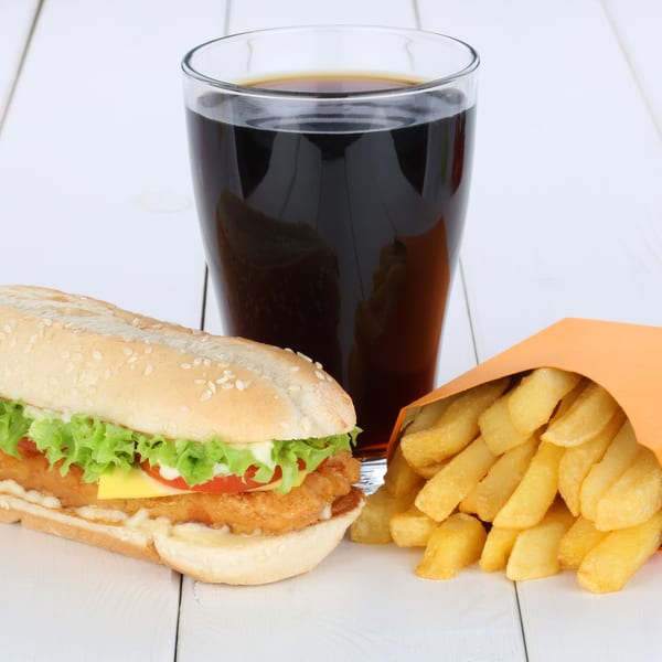 A Twin Acres-19th Hole chicken sandwich with fries and a soda on a white wooden table.