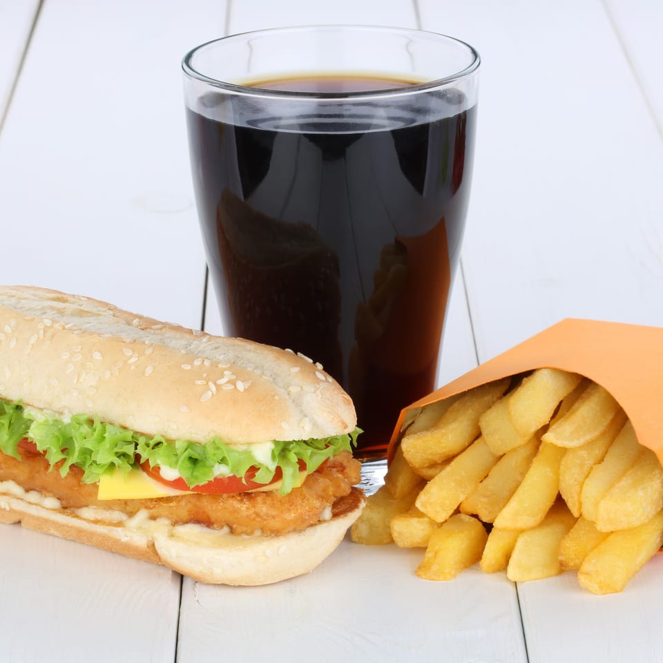 A Twin Acres-19th Hole chicken sandwich with fries and a soda on a white wooden table.