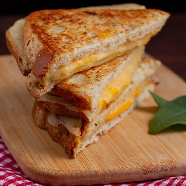 Stack of two grilled cheese sandwiches on toasted bread, with melted yellow cheese, on a wooden board.