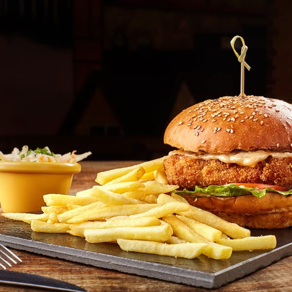 Crispy chicken sandwich with fries and coleslaw on a dark slate board at Twin Acres-19th Hole.